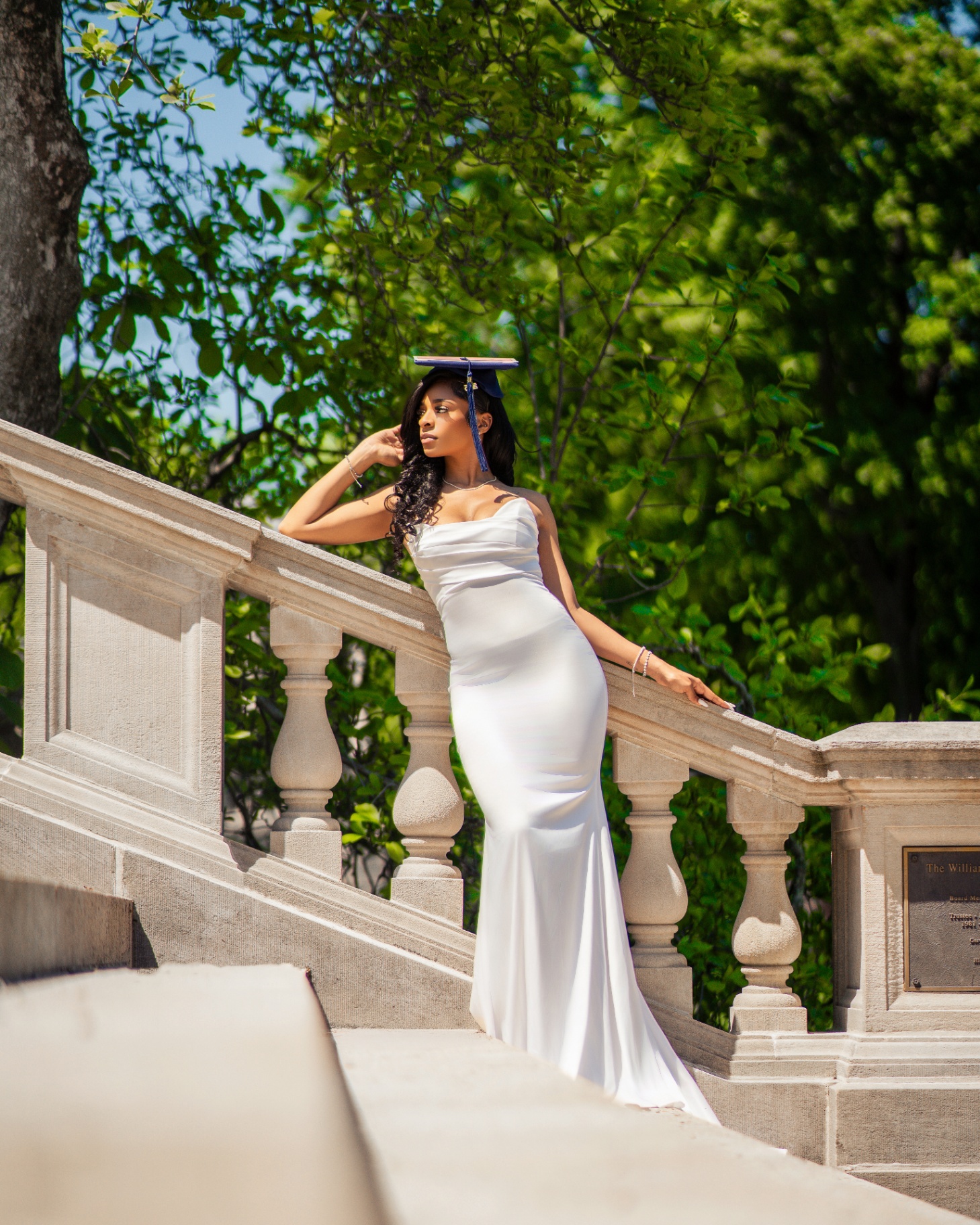 Grad in white satin gown leaning on stone balustrade