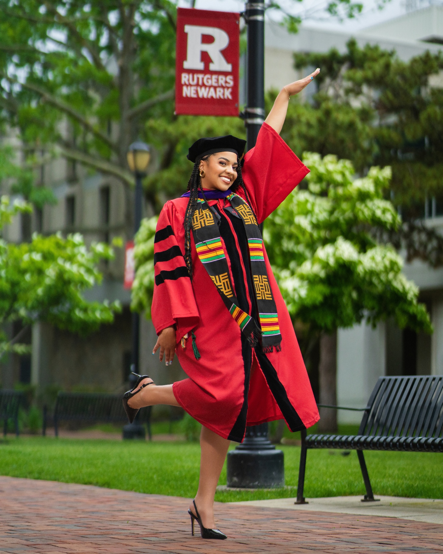 Rutgers Newark doctoral grad in red robe by campus banner