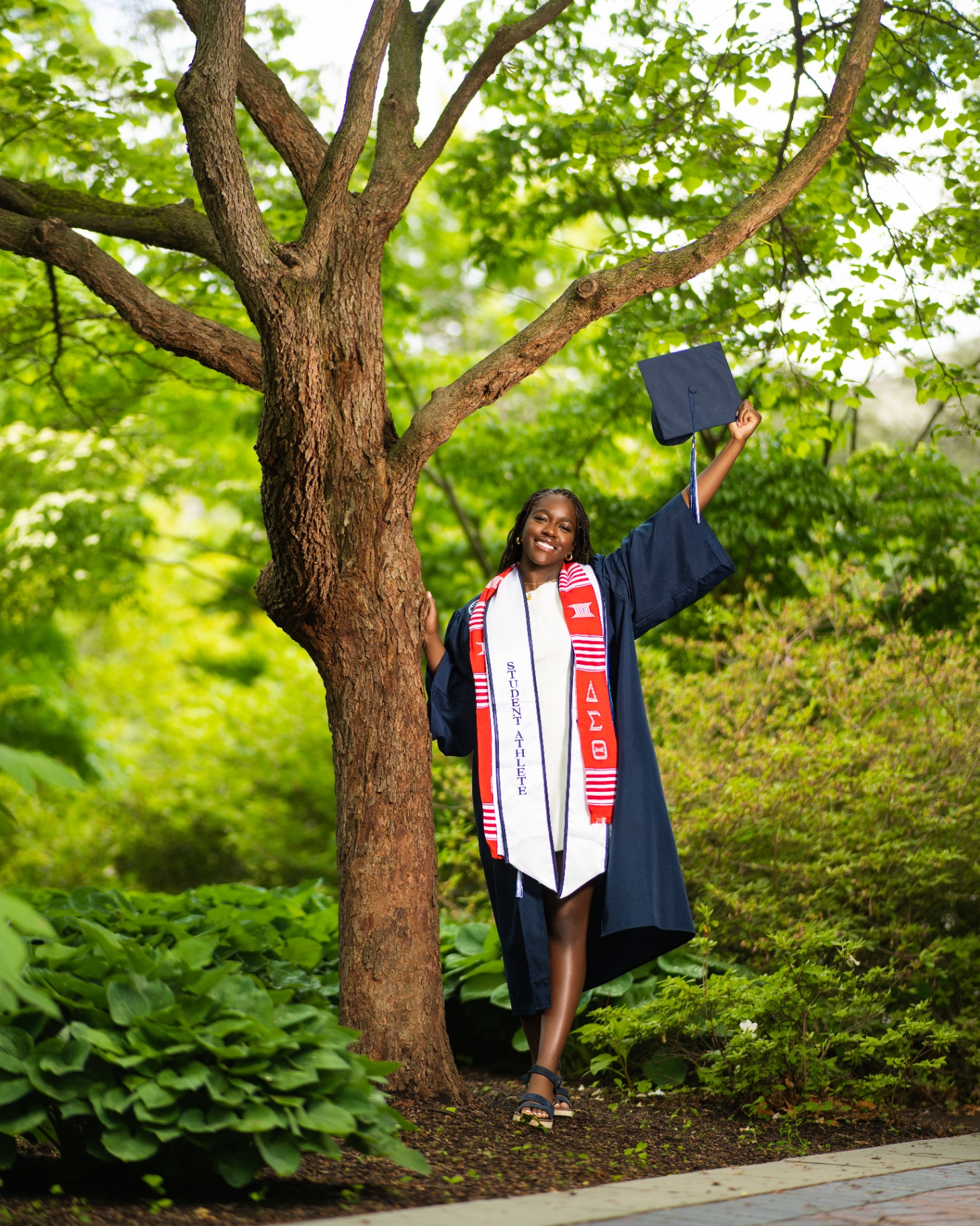 DST student athlete grad raising cap by a tree