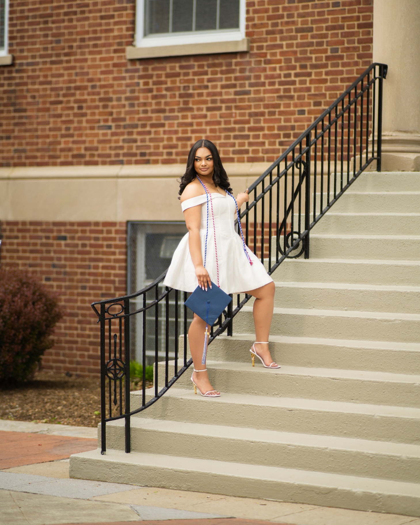 Grad in white dress on brick building staircase
