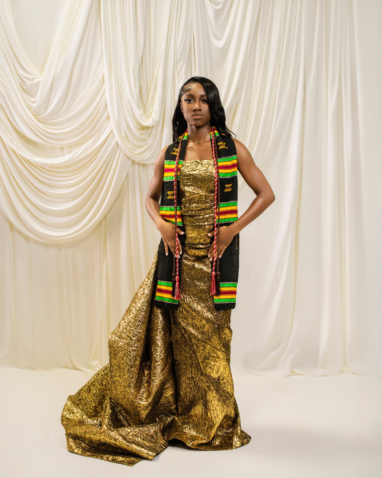 Grad in gold gown with kente stole and ivory drapes