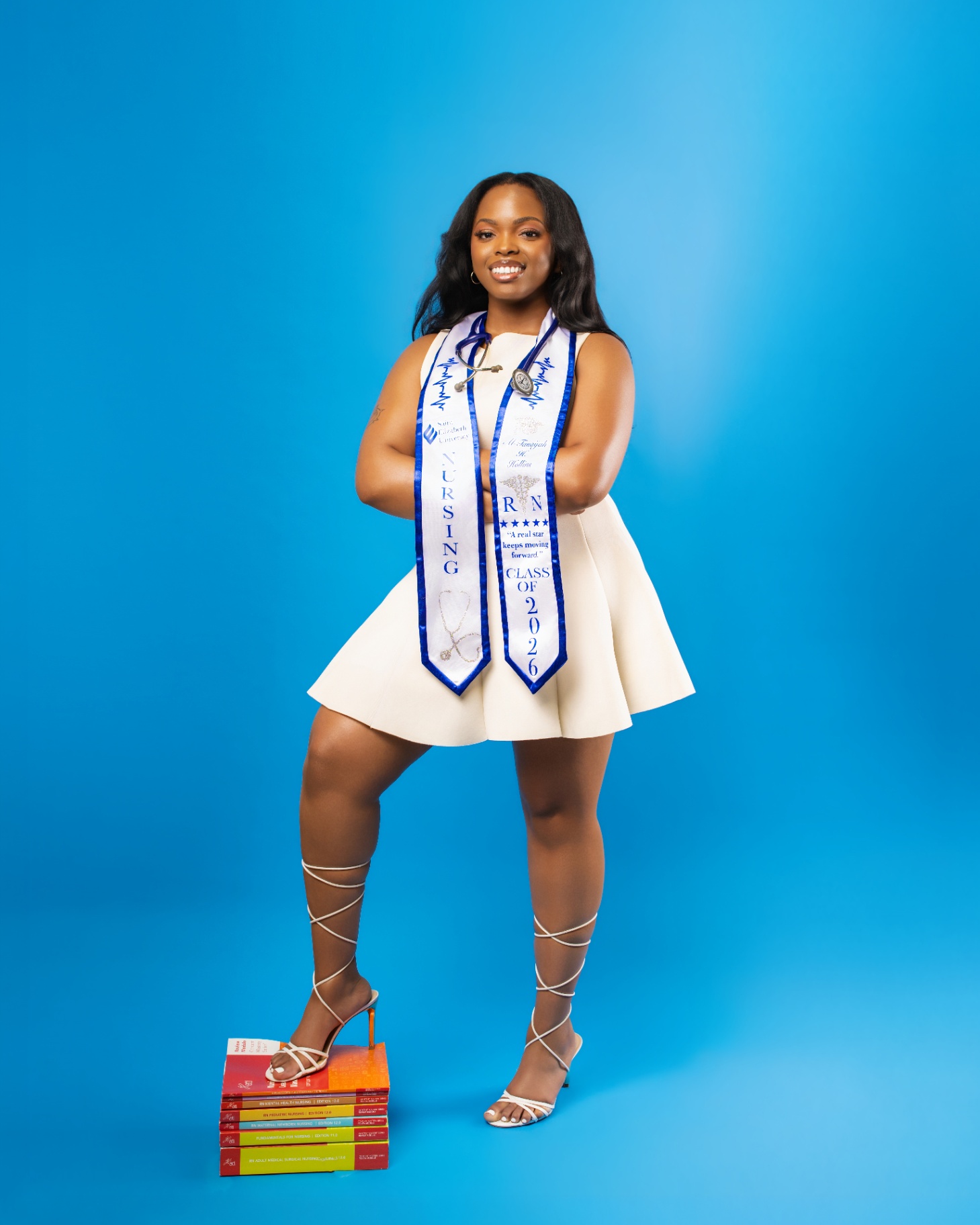 Nursing grad with stethoscope on stack of RN textbooks