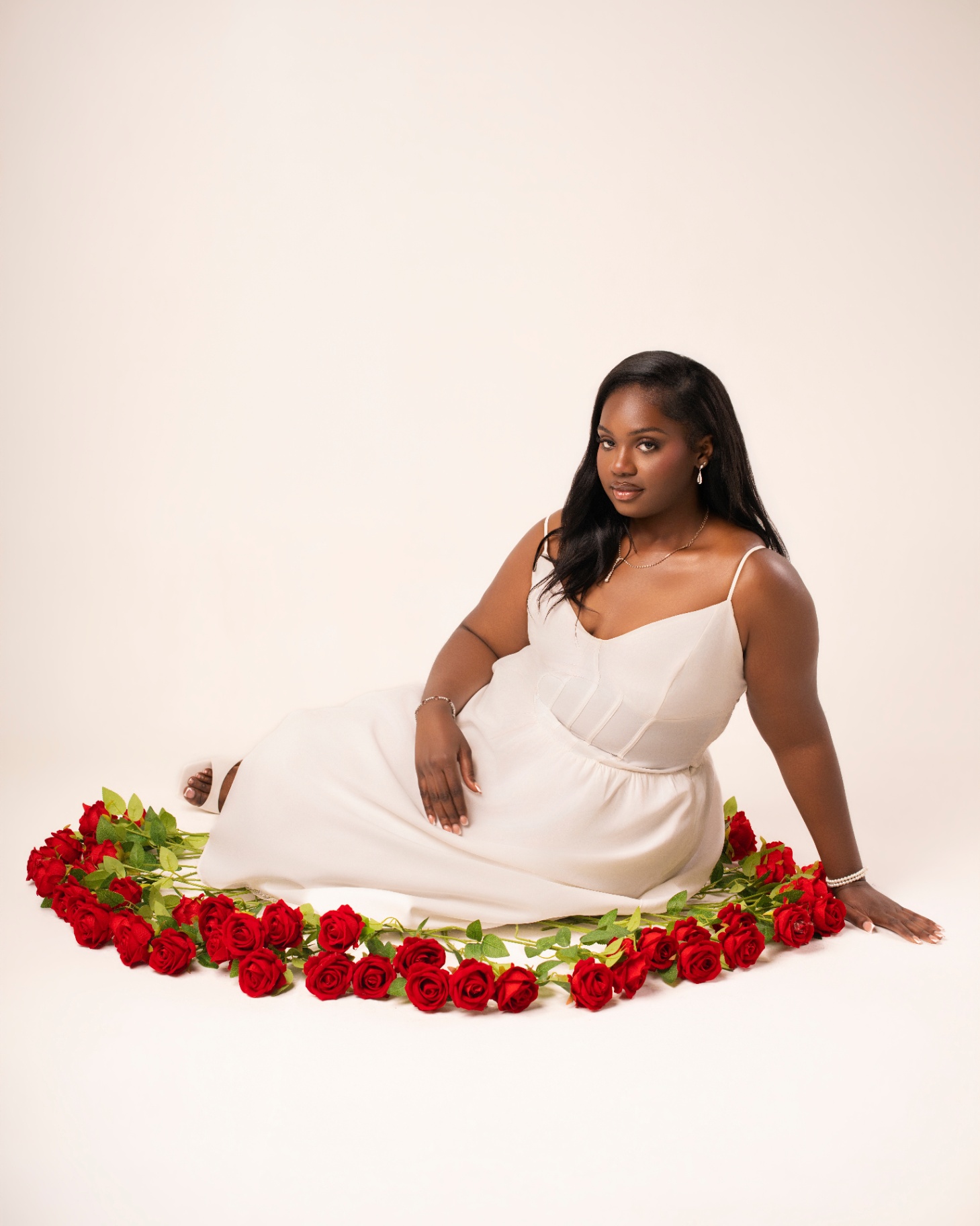 White gown seated in ring of red roses
