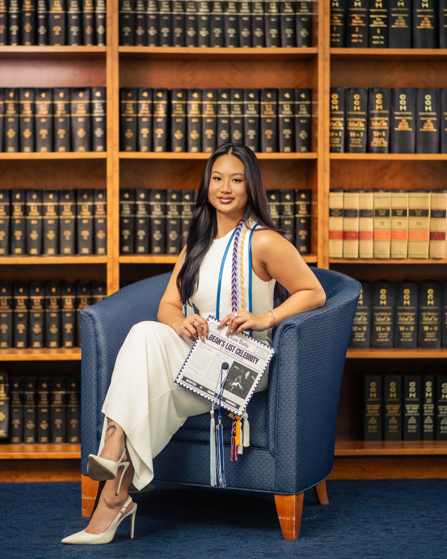 Business grad in white seated in law library with Dean's List cap