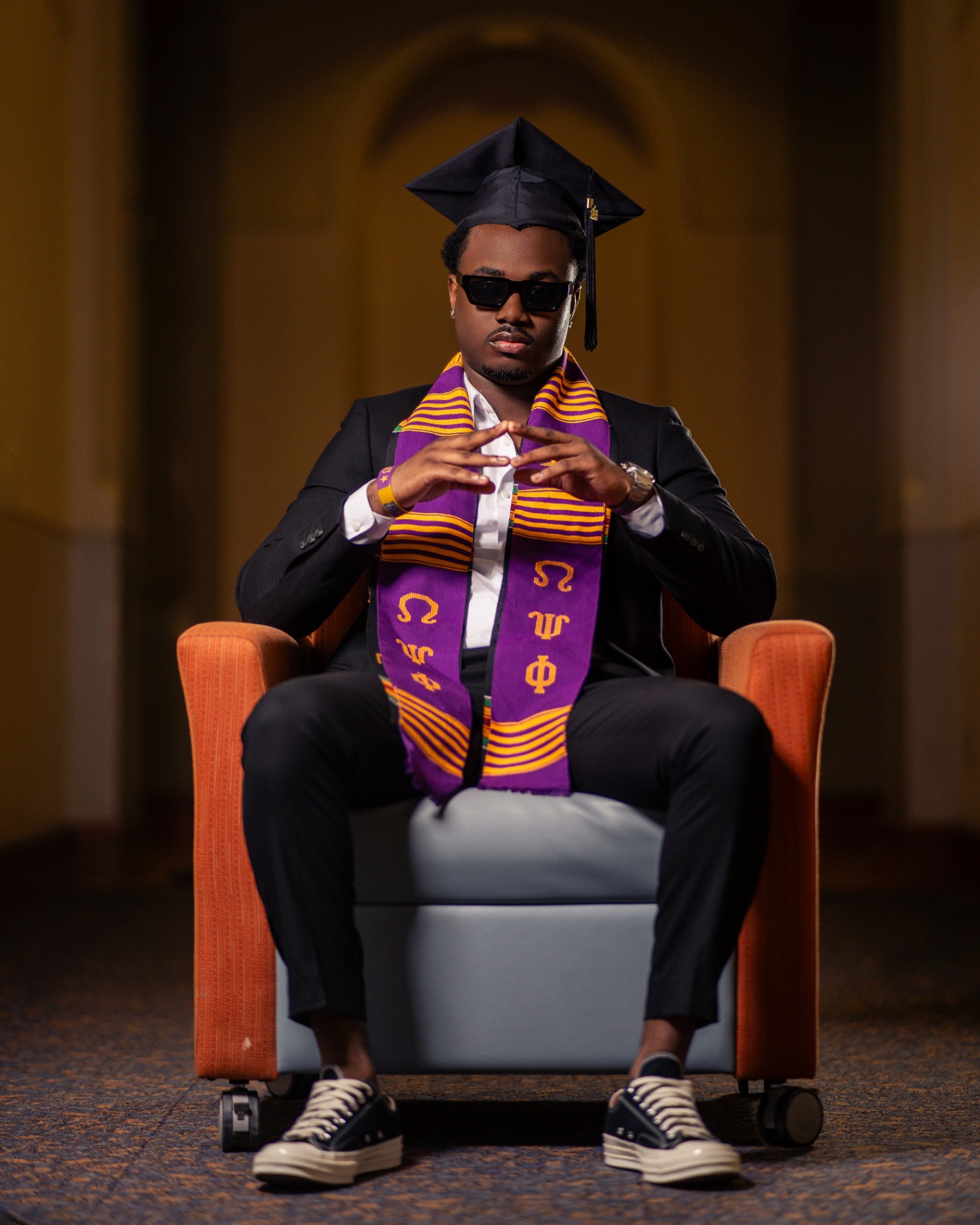 Omega Psi Phi grad seated with kente stole and shades