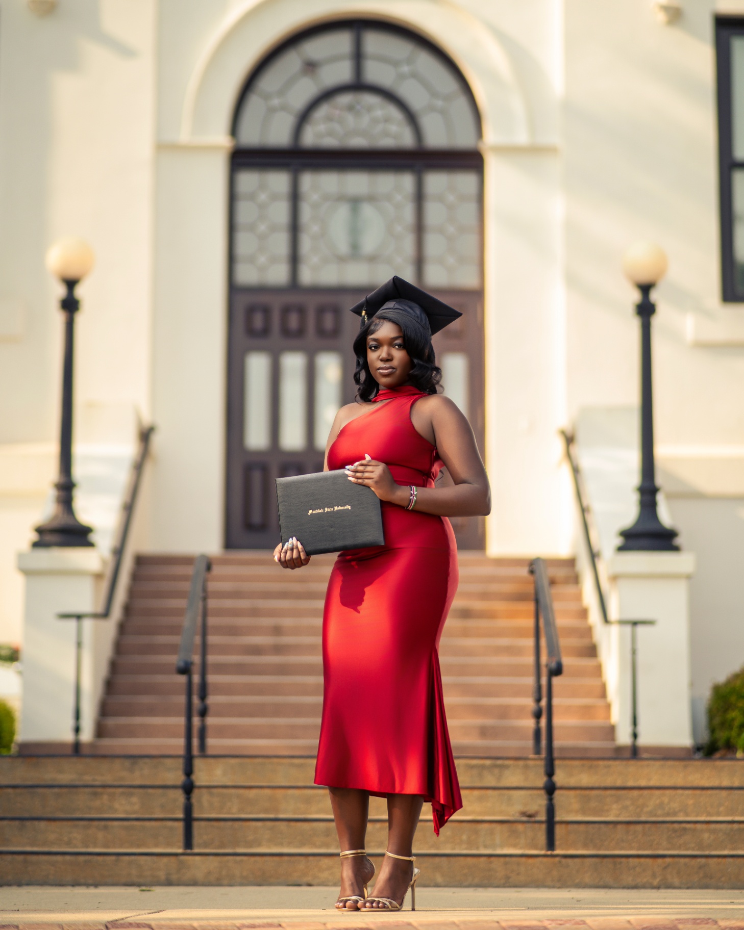 Graduate in red dress with diploma on campus steps