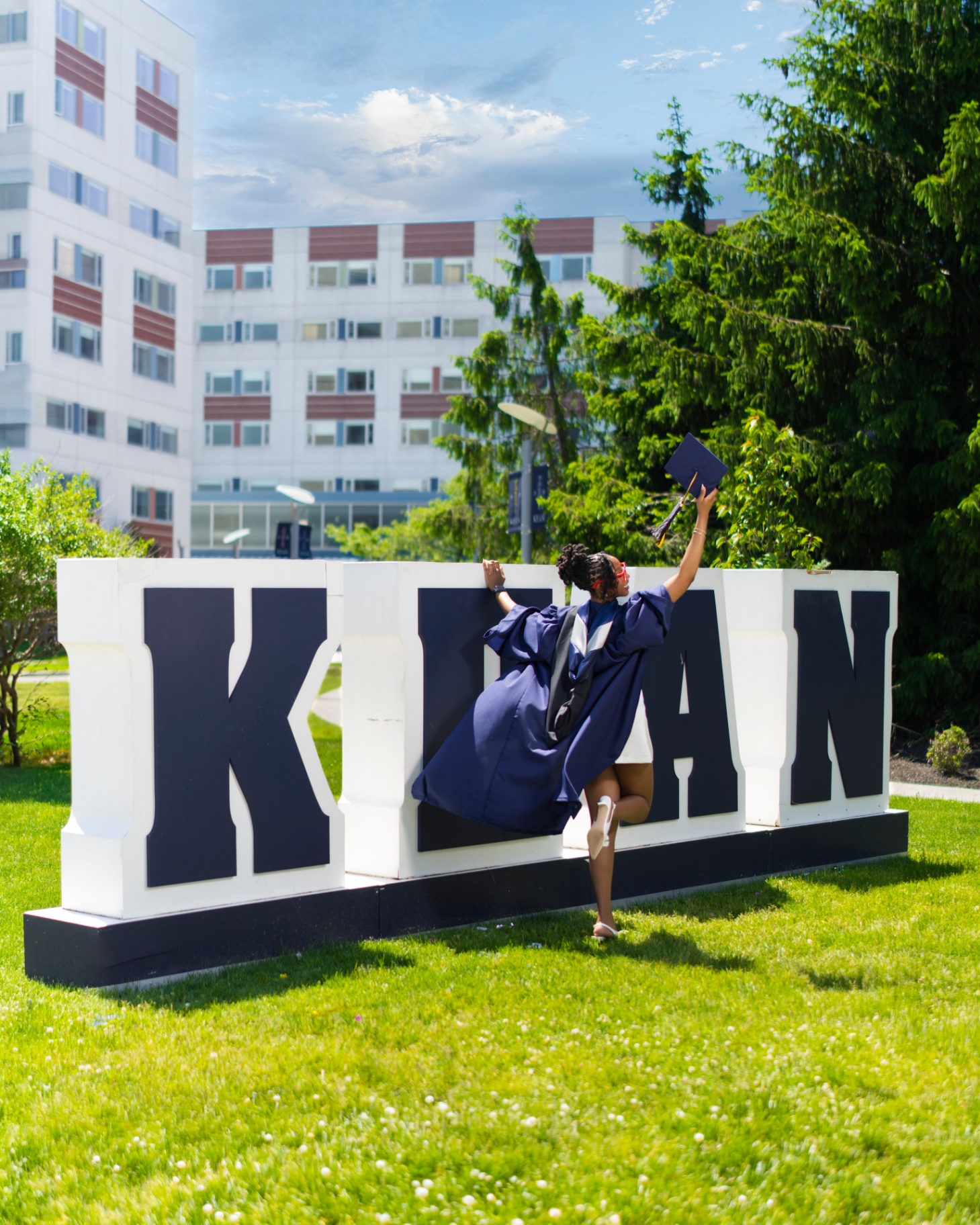Graduate in gown posing on Kean sign
