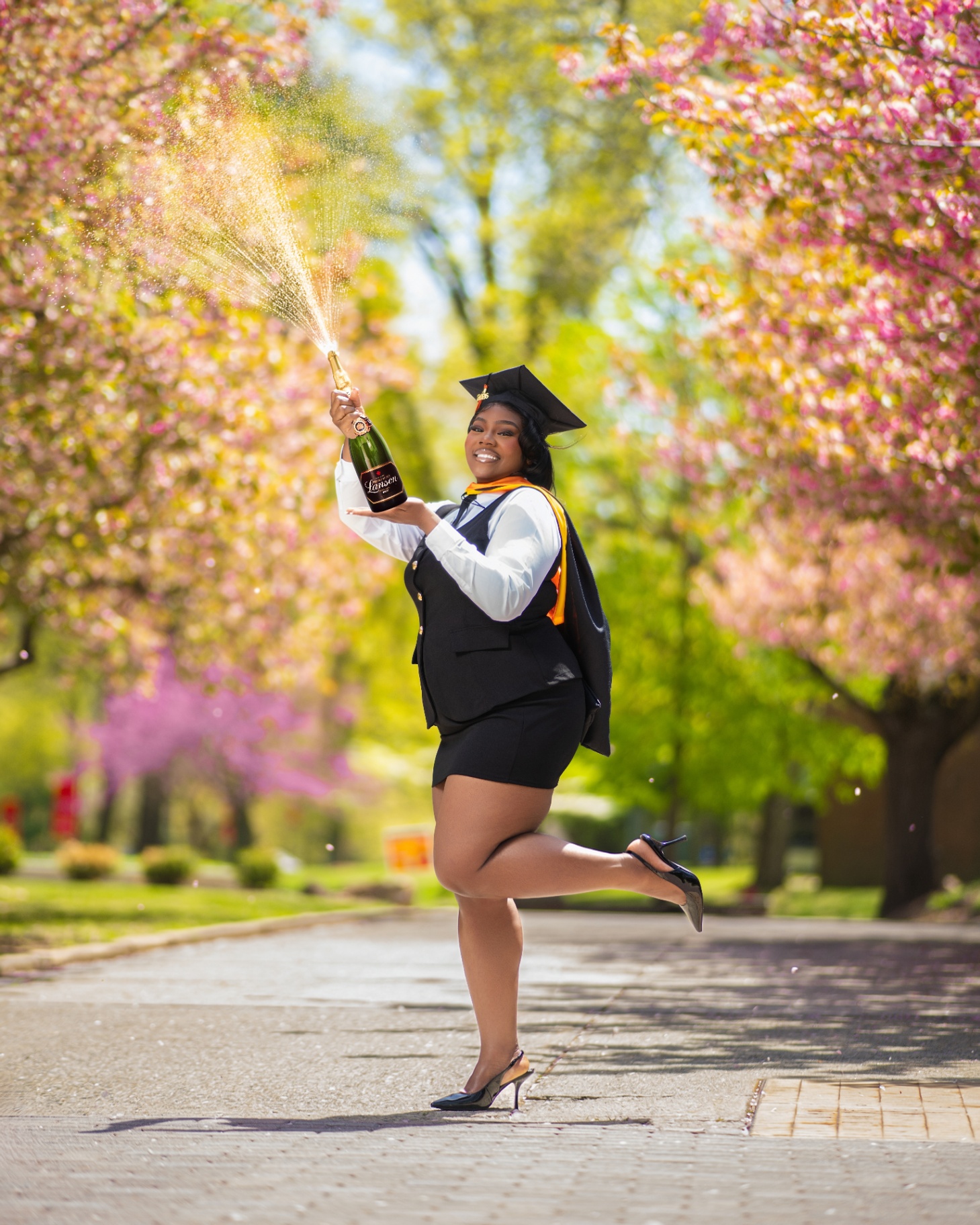 Graduate popping champagne under cherry blossoms