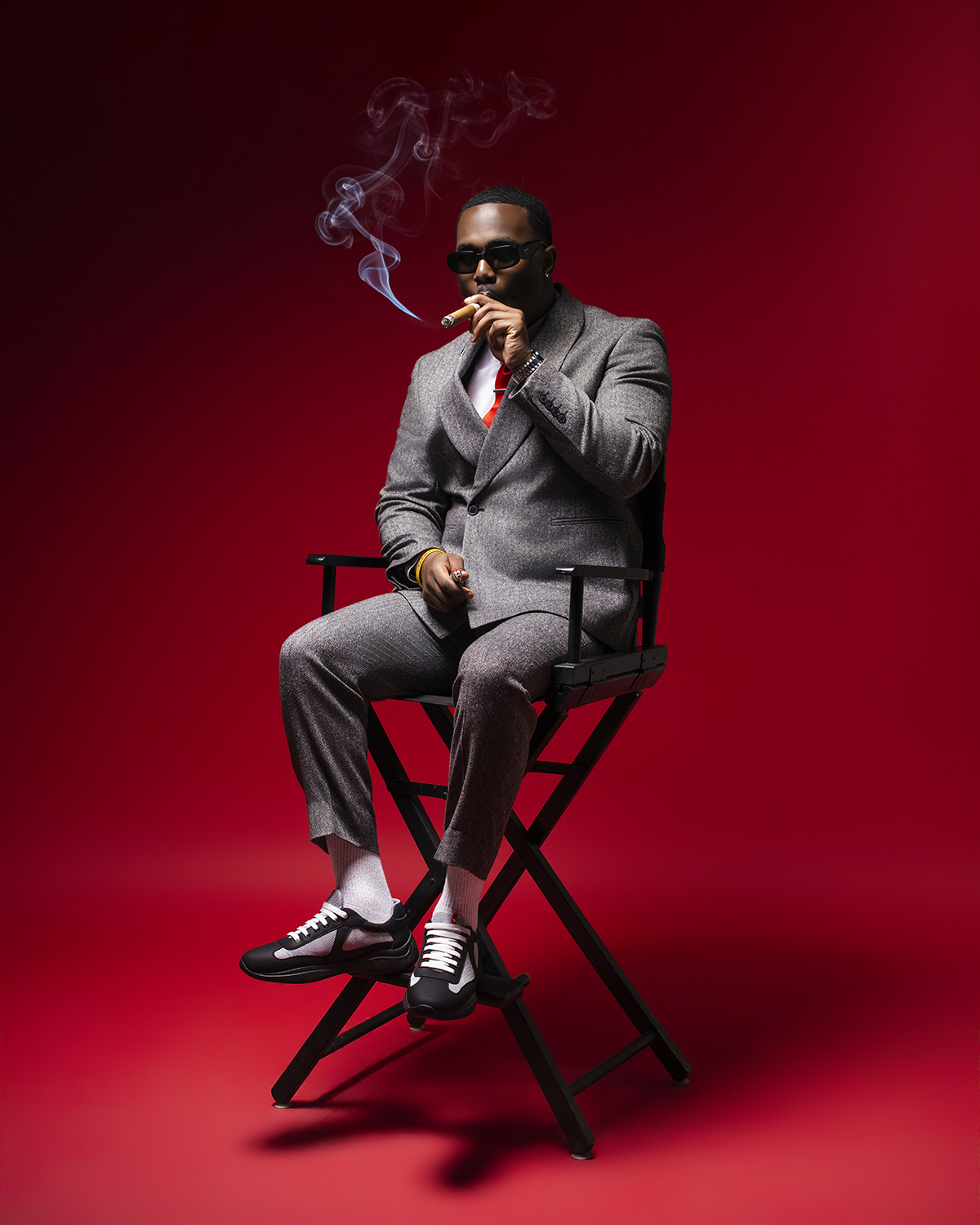 Grey suit seated with cigar on red backdrop