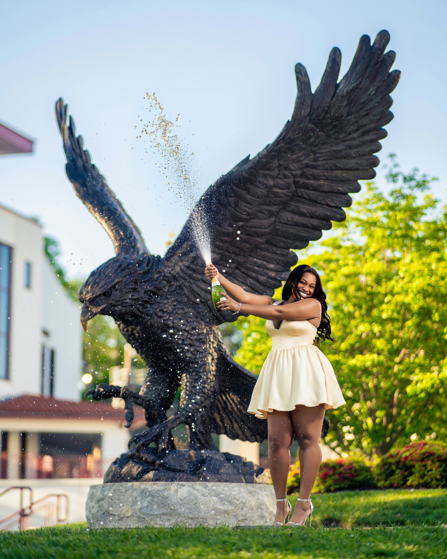 Grad popping champagne by giant eagle statue at sunset