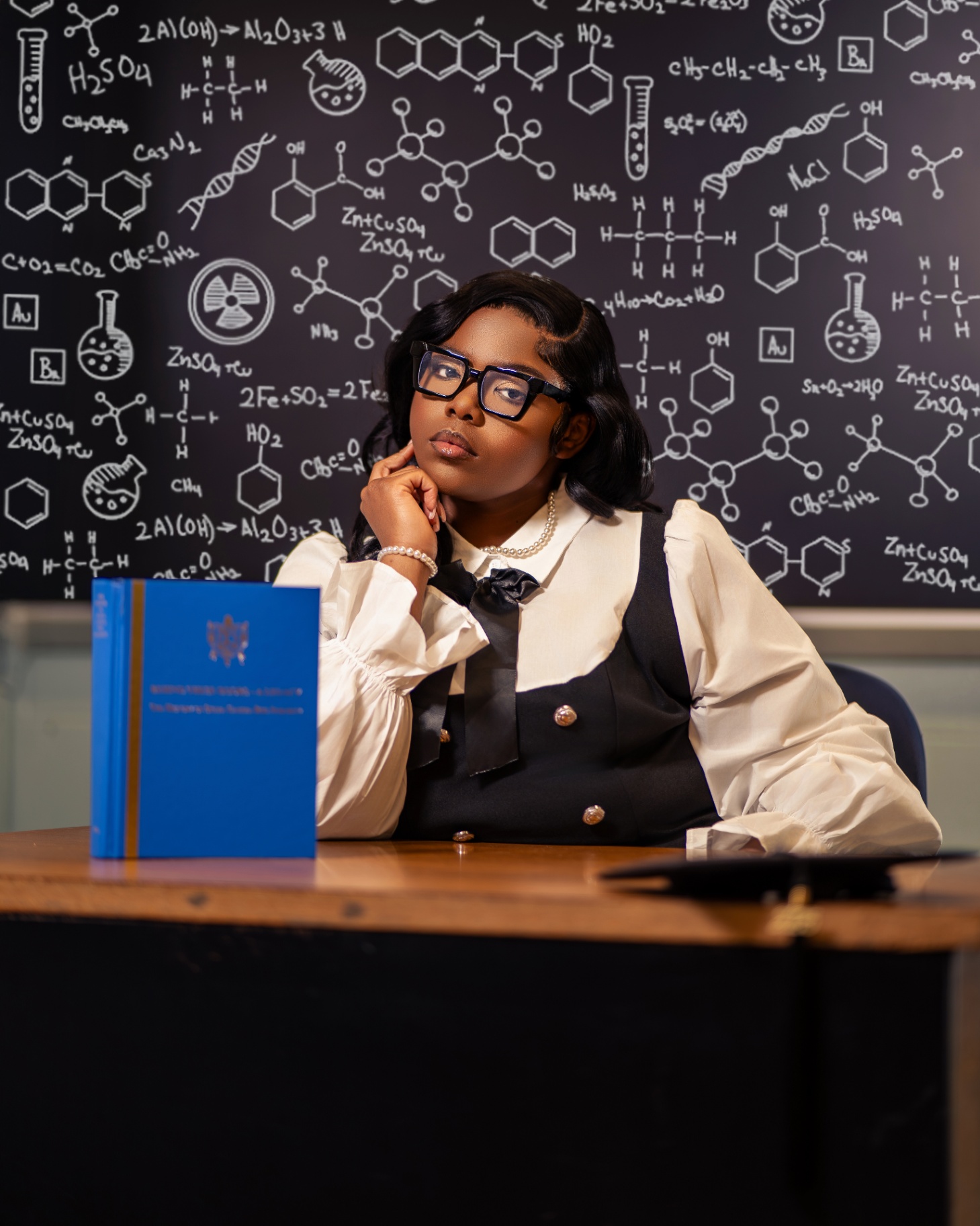 Chemistry grad at desk with formula chalkboard
