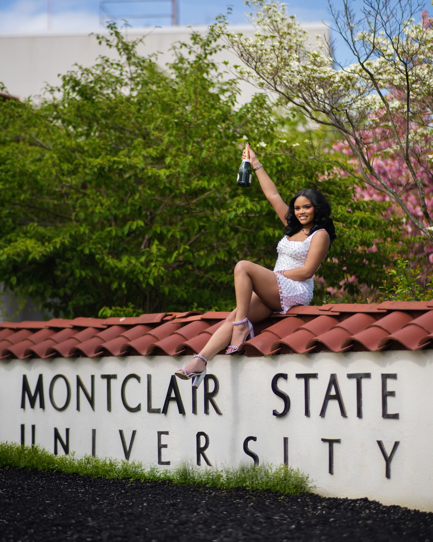 Graduate with champagne on Montclair State sign