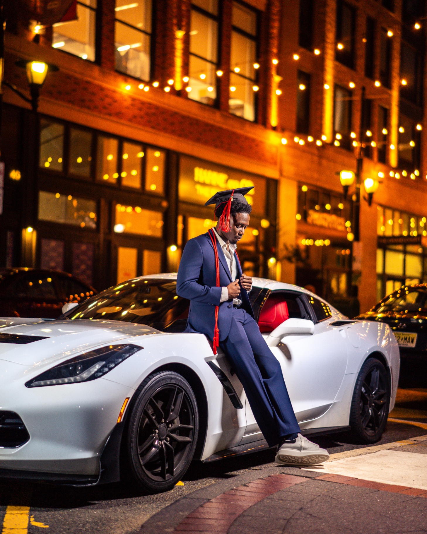 Grad in navy suit on white Corvette at night downtown
