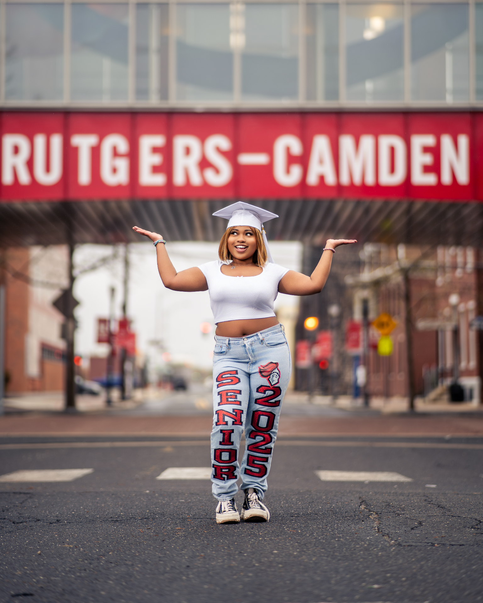 Rutgers-Camden senior in custom jeans posing under campus sign