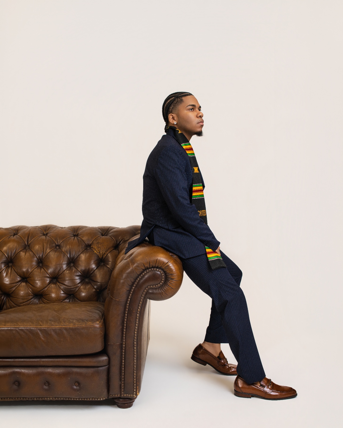 Graduate perched on Chesterfield sofa arm — profile