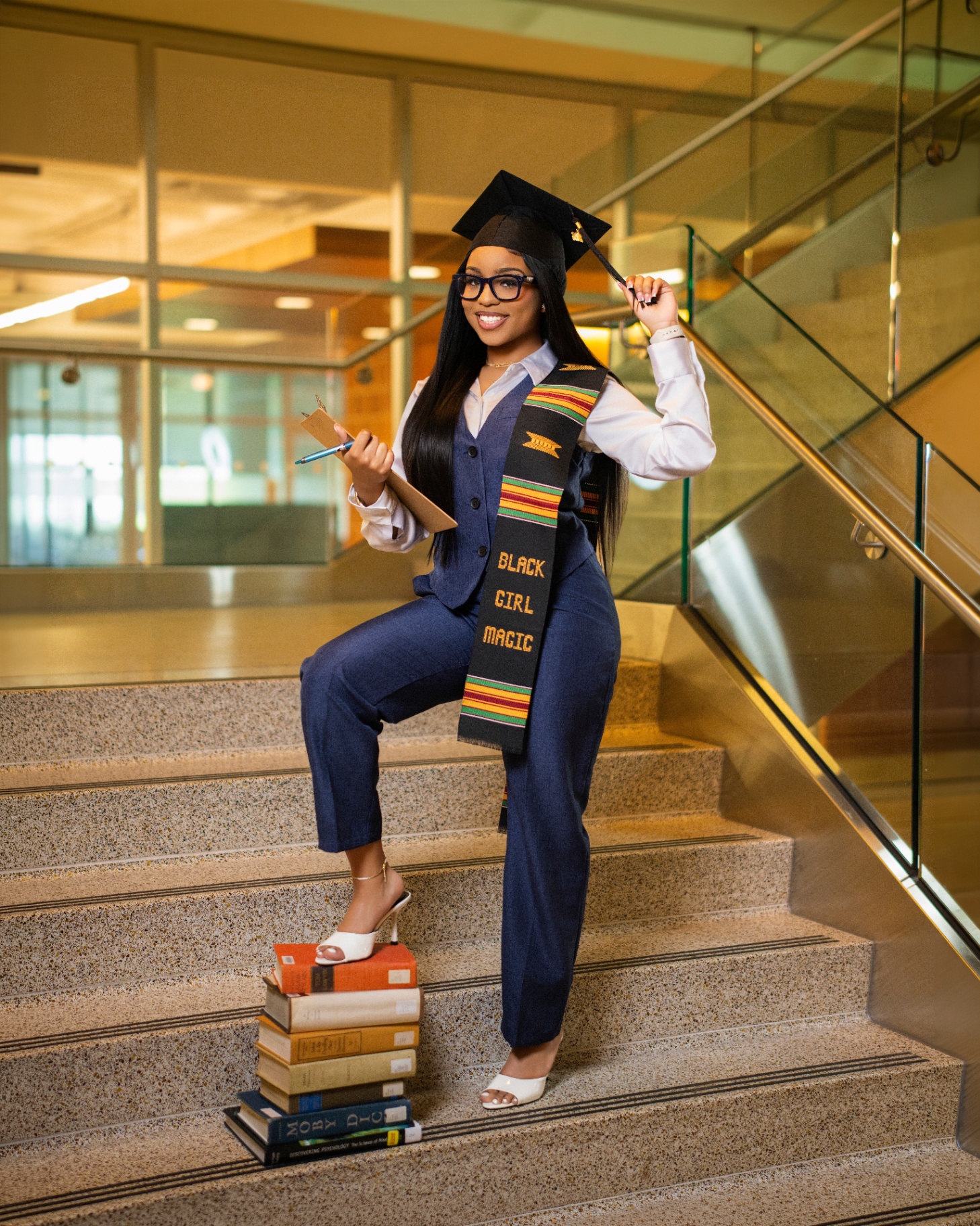 Black Girl Magic grad with books on campus stairs